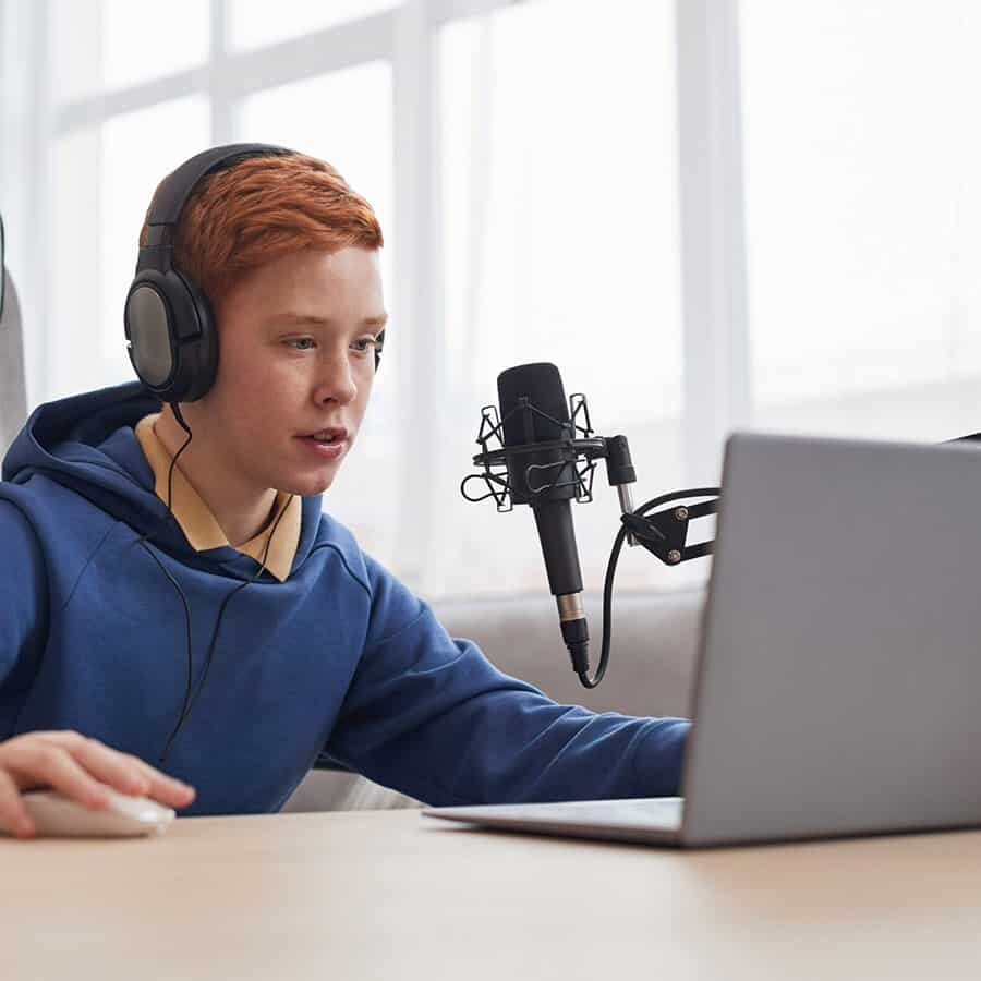 Portrait of red haired teenage boy playing video games with microphone and camera set up for online streaming, copy space